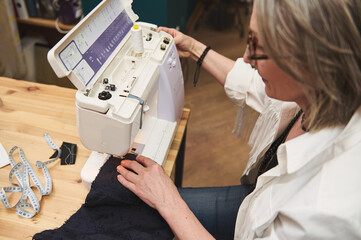 Close-up of a female tailor sewing clothes on sewing machine in tailoring atelier. Creation of new garment, fashion designer business start-up concept