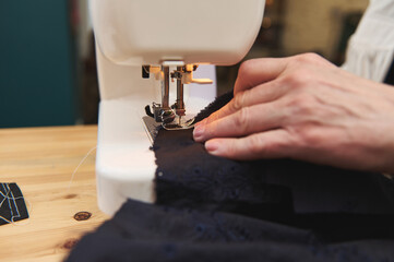 Close-up of women's hands behind her sewing on a sewing machine while creating handmade collection of new clothes