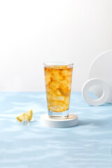 Iced tea with lemon in highball on white podium and blue table. Refreshing lemonade, ice tea.