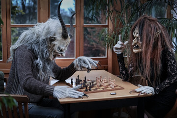 Mature man and woman in ghost costume playing chess game sitting at table