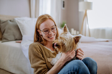 Cheerful woman with pet dog sitting by bed at home