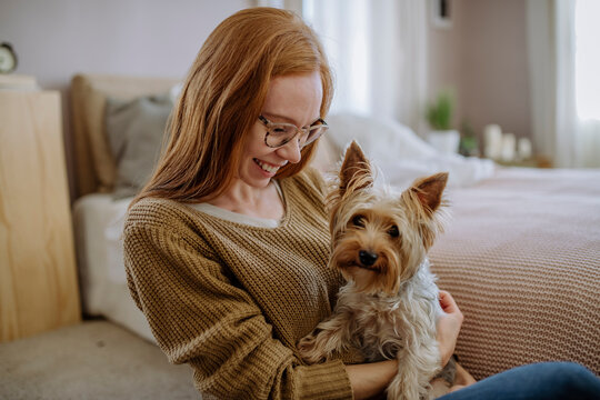 Happy woman with pet dog sitting by bed at home