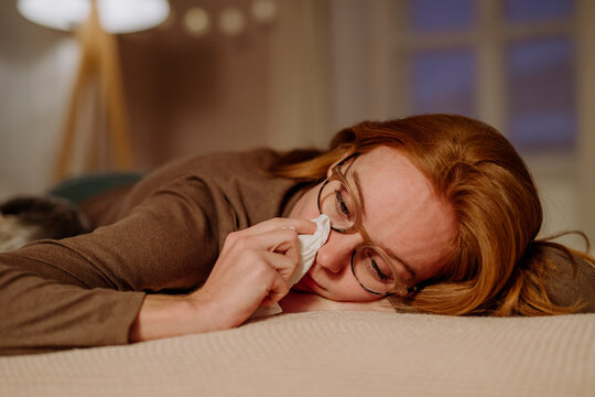 Sad redhead woman with tissue paper crying on bed at home