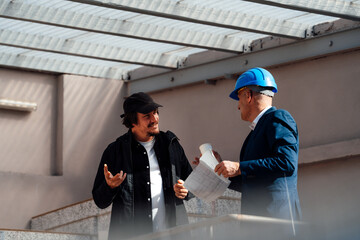 Senior architect holding blueprint discussing with employee in construction site