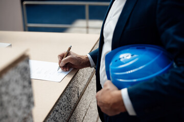 Businessman holding blue hardhat signing document