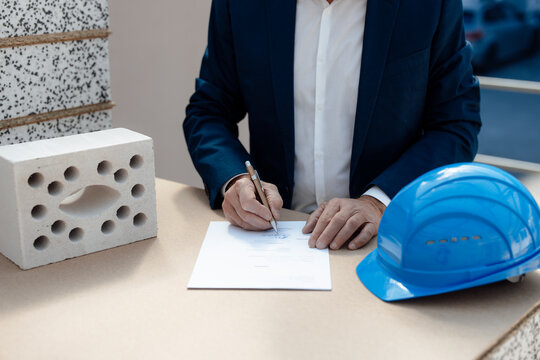 Senior businessman signing document amidst concrete brick and hardhat at construction site