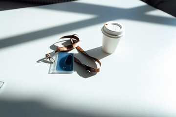 ID Card and disposable cup on white desk in sunlight