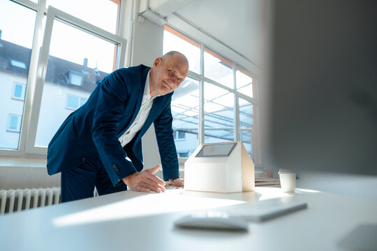 Smiling senior engineer with solar panel on model house in office