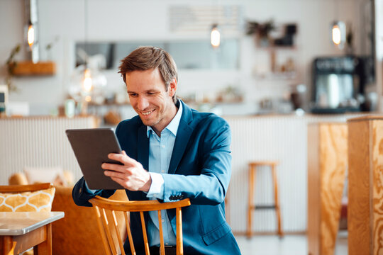 Happy businessman sitting on chair and using tablet PC at cafe