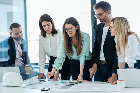 Businesswoman discussing plan over documents with colleagues at desk in office