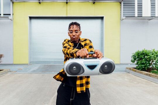 Young man wearing eyeglasses dancing with boom box in front of shutter