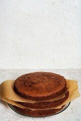 Chocolate sponge flourless cake layers with bake paper, light background. Brownie cake