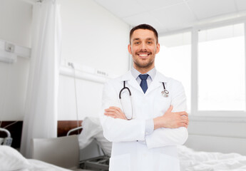 medicine, profession and healthcare concept - smiling male doctor with stethoscope over hospital ward background