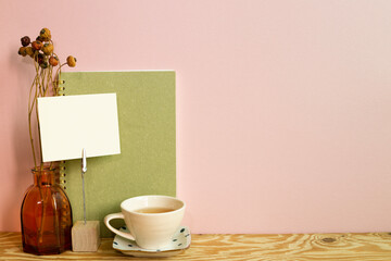 Memo holder and notebook, cup of tea, dry flowers on wooden desk. pink wall background. workspace