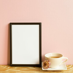 Picture frame and cup of tea on wooden table. pink wall background. copy space