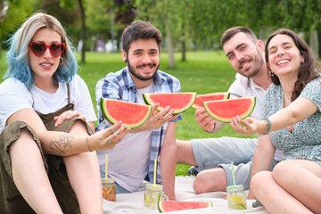 Group of happy friends smiling and looking at camera with watermelon in the park having picnic on a sunny summer day.