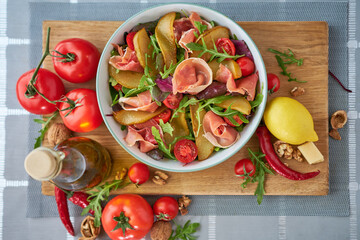 Salad with jamon or prosciutto, pears, tomatoes and arugula on wooden board