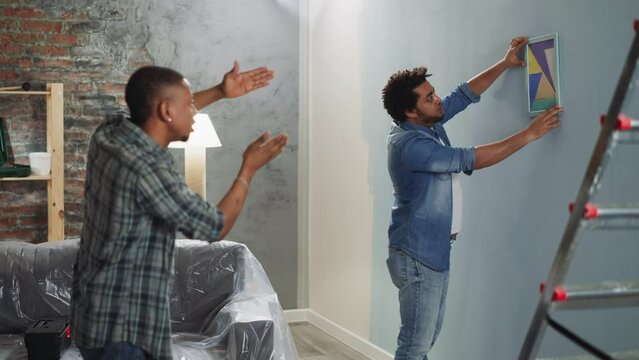 Black guy advises brother to turn abstract picture on wall