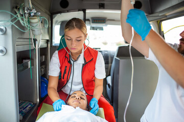 Medics with injured patient giving an infusion . Young male paramedics holding iv solution. Female doctor listeting heart of patient © Graphicroyalty