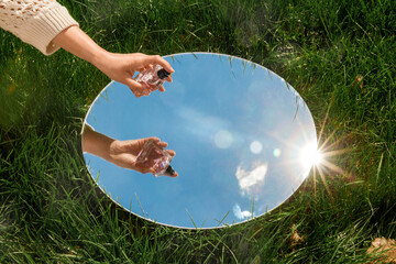 perfumery and nature concept - hand with bottle of perfume and sky reflection in round mirror on...