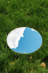 nature concept - blue sky and cloud reflection in round mirror on grass