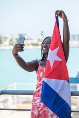 Woman holding cuban flag taking a selfie with the sea and the city behind