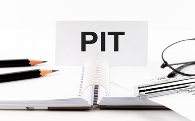 Text PIT on paper card,pen, pencils, glasses,financial documentation on table - business concept