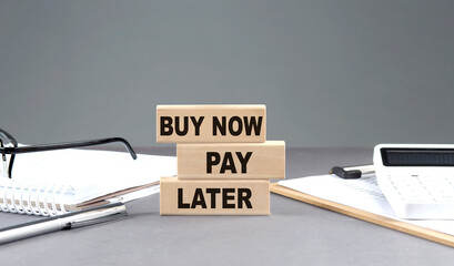 BUY NOW PAY LATER text on wooden block with notebook,chart and calculator, grey background