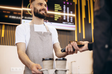 Male barista holding terminal while customer paying with card