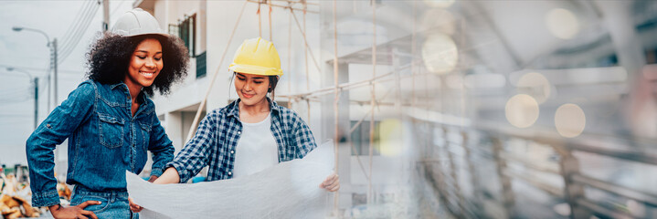 Young female architector and engineers with draft plan of building talking on constructing site. Banner cover design.