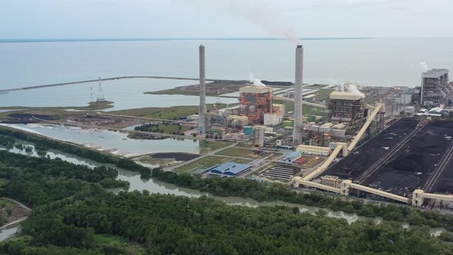 Aerial shot of coastal coalfield, industrial ultra-supercritical coal-fired power plant with smokes raising from chimney located at lekir bulk terminal jalan, teluk rubiah, manjung, perak, malaysia.