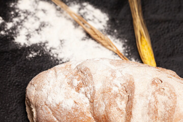 Loaf of bread with wheat ears and flour on a black background, top view