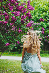 A beautiful curly woman in a summer dress runs and rejoices, she is wearing sunglasses. Against the background of a purple lilac bush