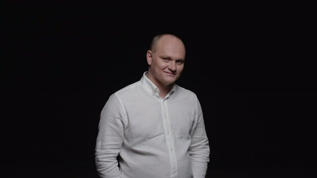 A bald man in a white shirt poses for the camera on a black background.