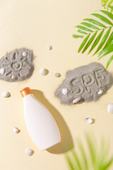 Sunscreen bottle on yellow background with sand, seashells and palm leaves. Cosmetics for safe sunburn. Sun protection cream with SPF. Skin care.