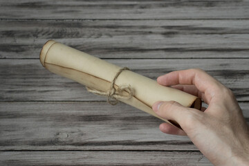 Man holds in his hand an ancient rough scroll against a wooden surface.