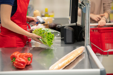 Unrecognizable woman buying foods in modern supermarket, cashier beeping them