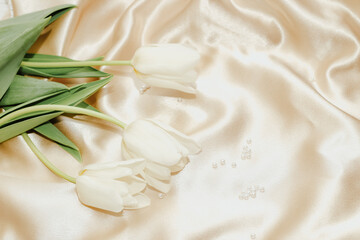 Fototapeta na wymiar Bouquet of white tulips with pearl beads on silk golden nude satin background.