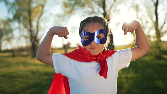 Girl in red superhero cape play in park. Family happiness. Child dream of becoming champion. Strong will to win.Girl in superhero mask on summer vacation. Child plays in park. Happy family concept