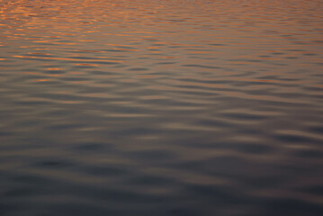 Calm smooth water on sunset with orange, pink, yellow reflection and glare of sun on blue water, texture, background.