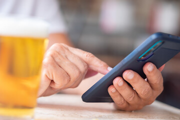 Closeup on female hands using phone for messaging, close to a glass of beer