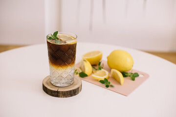 Delicious refreshing espresso tonic cocktail standing on the table, garnished with ice and lemon,...
