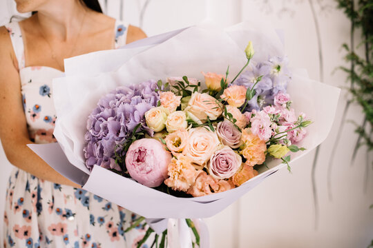 Very nice young woman holding big and beautiful bouquet of fresh hydrangea, peony, roses, eustoma, carnations in peach and lavender colors, cropped photo, bouquet close up