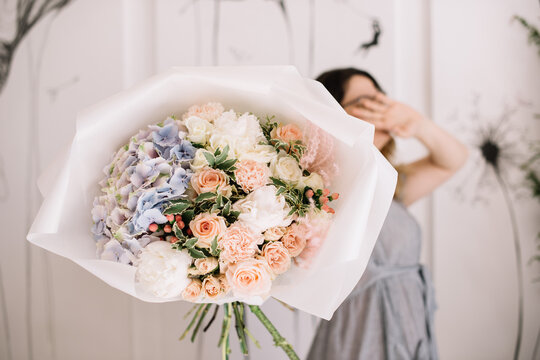 Very nice young woman holding big and beautiful bouquet of fresh hydrangea, roses, peony in blue and pink colors, cropped photo, bouquet close up