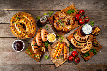 Mix bar-b-q sausages - bavarian, round, gumberland, bratwurst with ketchup, mustard barbeque sauce. Various bbq grilled sausages flat lay on wood background. Street festival grill food menu.