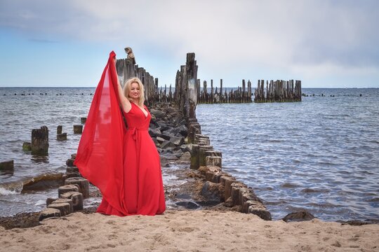 Interesting holiday seaside concept. Beautiful woman in a red dress on the seashore.