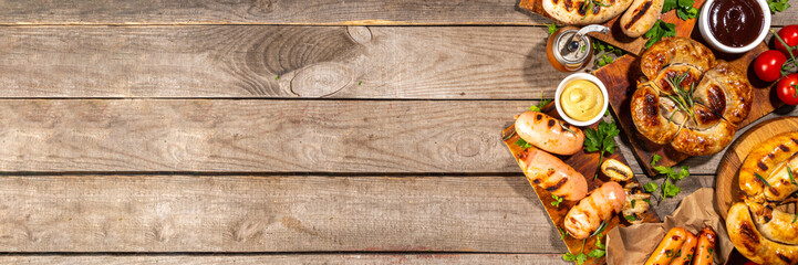 Mix bar-b-q sausages - bavarian, round, gumberland, bratwurst with ketchup, mustard barbeque sauce. Various bbq grilled sausages flat lay on wood background. Street festival grill food menu.