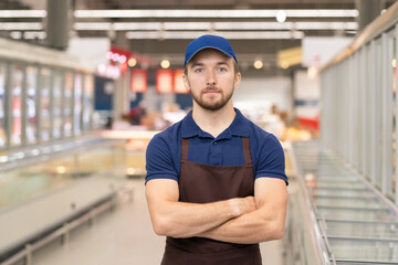 Horizontal medium portrait of modern young man wearing uniform working in store standing with arms crossed looking at camera
