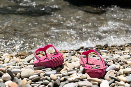 Chanclas rosa sobre guijas en la orilla de la playa