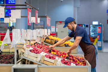 Side view shot of man wearing apron working in store setting out fresh fruits, copy space